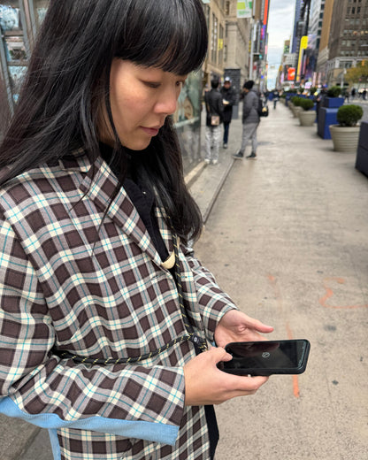Woman standing in the street wearing a crossbody phone strap by TOIA, browsing her phone. 