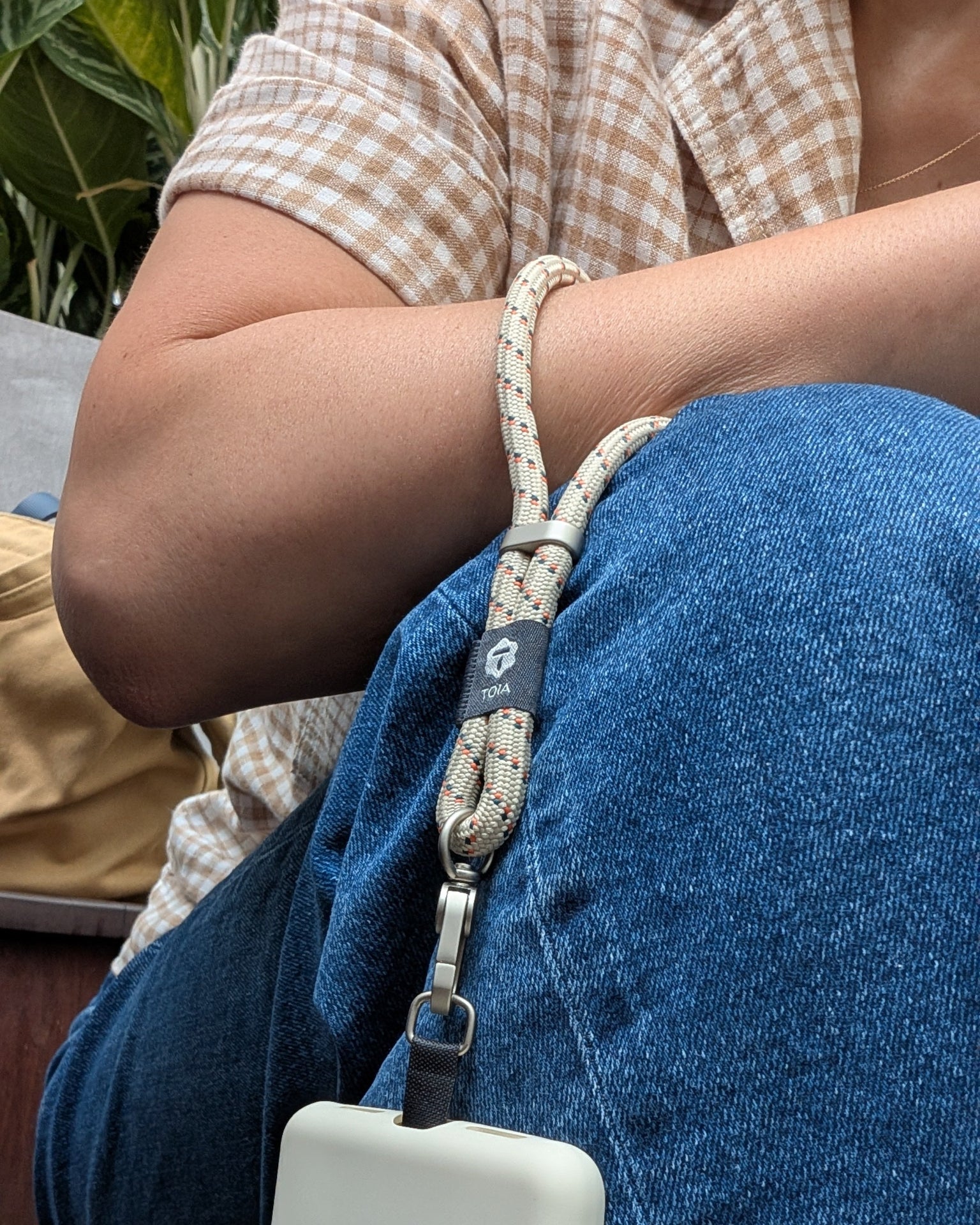 Person holding a toia wrist strap over their knee, wearing blue jeans.