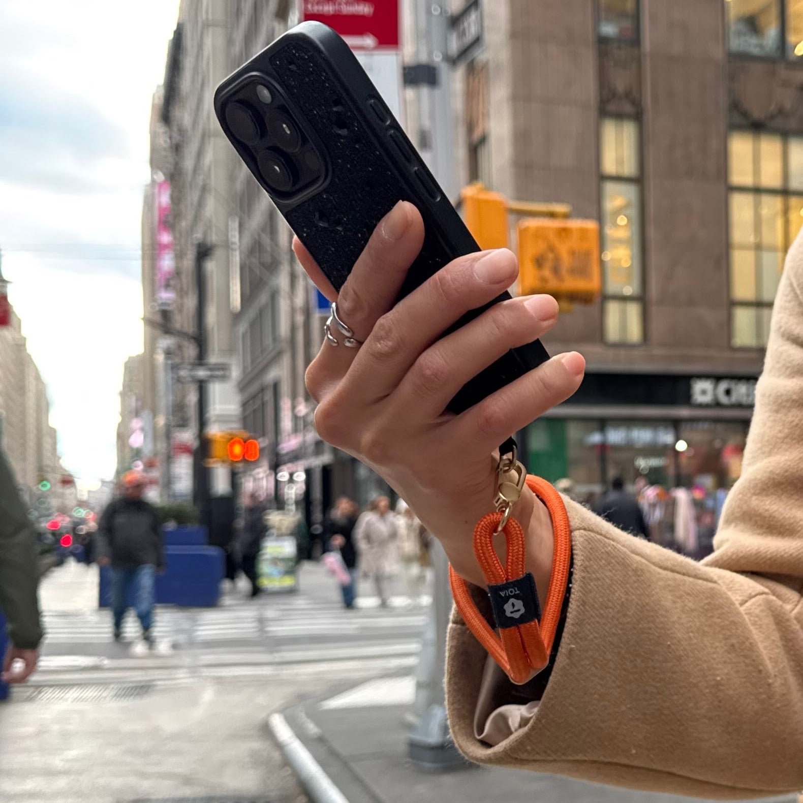 Person holding a phone attached to an orange wrist phone strap by TOIA.
