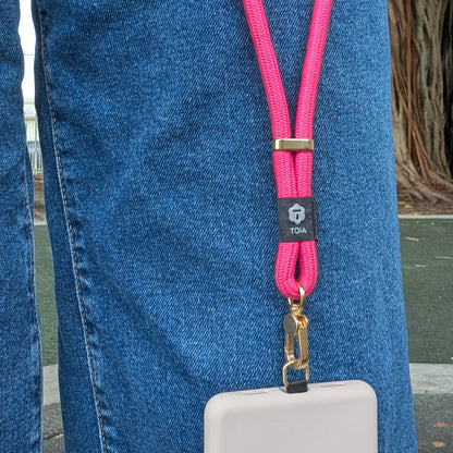 Vibrant hot pink wrist strap by TOIA attached to a phone against a pair of denim jeans.