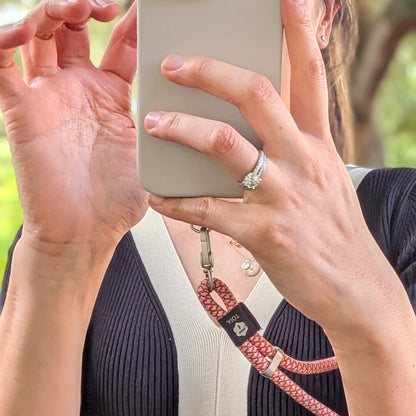 Woman holding a phone attached to a red and white woven rope wrist phone strap by TOIA.